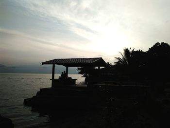 Silhouette building by sea against sky at sunset