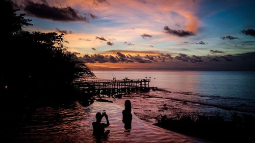 Silhouette people on beach against sky during sunset