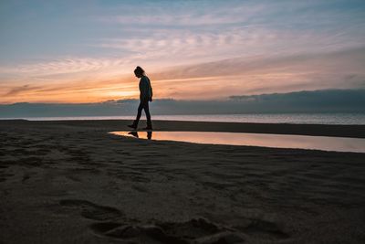 Silhouette man standing on beach against sky during sunset