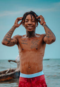 Portrait of shirtless man standing at beach against sky