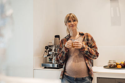 Expectant woman holding tea cup standing in kitchen at home