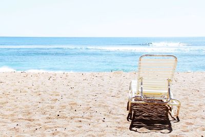 Empty chair at beach against clear sky