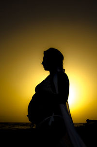 Silhouette pregnant woman standing against sea and sky during sunset