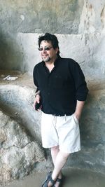 Man wearing sunglasses while standing against stone wall