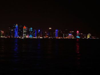 Illuminated buildings by river against sky at night