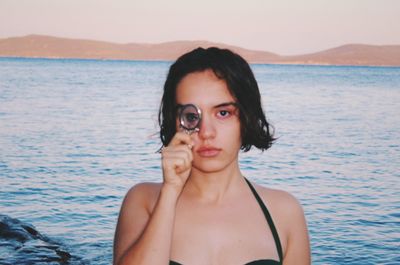 Portrait of beautiful young woman standing at beach against sky