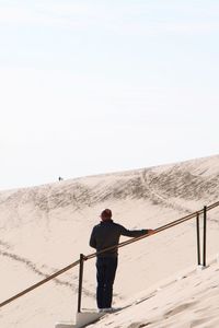 Rear view of mature man standing on sand at beach against clear sky during sunny day