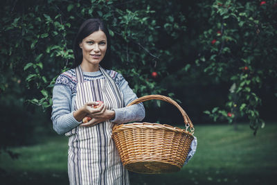 Portrait of woman carrying wicker basket at apple orchard