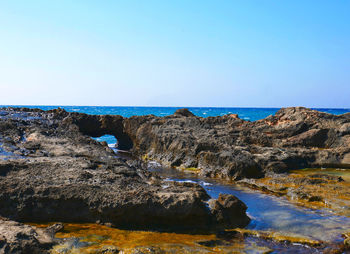 Rocks by sea against clear sky
