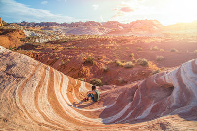 Woman sitting on mountain against sky