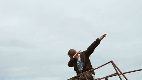 Low angle view of man standing on railing against sky