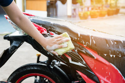 Cropped hand of woman washing motor scooter outdoors