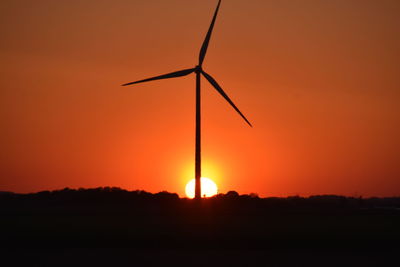 Silhouette of wind turbines on field against orange sky