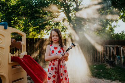 Young girl spraying mist from garden hose in backyard
