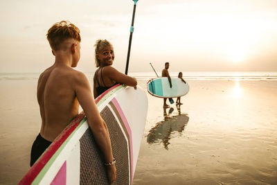 Family with paddleboards walking towards sea during sunset at beach