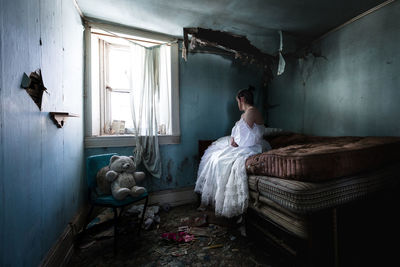 Rear view of woman sitting on bed at home