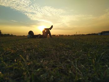 Man and dog on field against sky during sunset