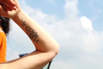 Cropped hand of woman with tattoo against sky