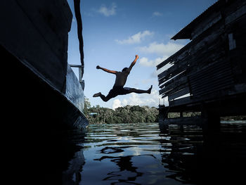 Man jumping over lake against sky