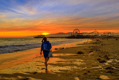 Rear view of woman on beach against sky during sunset