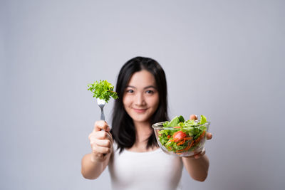 Portrait of young woman holding food against white background