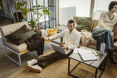 High angle view of programmer using mobile phone sitting with laptop on carpet in creative office