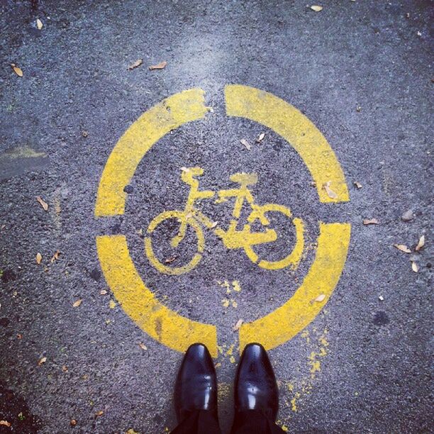 low section, personal perspective, person, shoe, street, road marking, high angle view, standing, road, human foot, unrecognizable person, men, asphalt, lifestyles, yellow, transportation, text