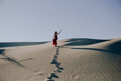 Full length of woman in red dress walking on desert against clear sky