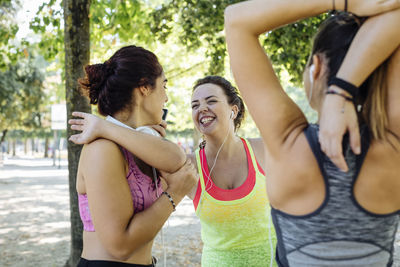 Young female friends laughing while doing warm up exercise in park