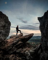 Man standing on rock by sea against sky