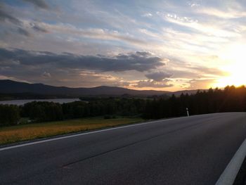 Road by landscape against sky during sunset