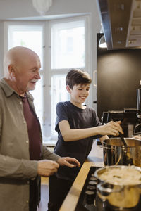 Smiling grandson preparing food with grandfather in kitchen at home