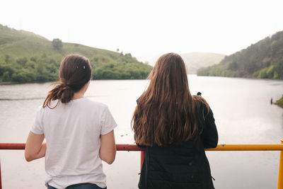Two sisters looking away on bridge over lake