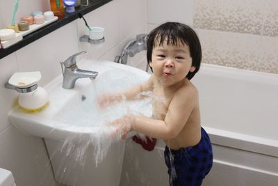 Portrait of cute boy playing in running water on wash bowl