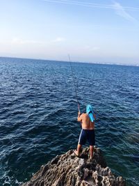 Man fishing in sea against sky