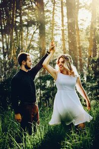 Young woman with arms raised on field in forest