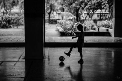 Silhouette boy playing with ball in dark hallway