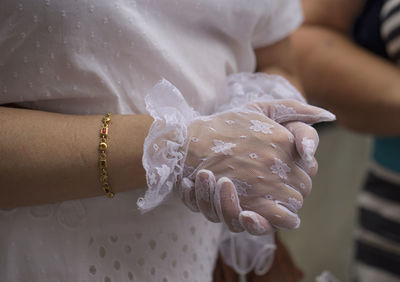 Midsection of bride with hands clasped in wedding dress by woman