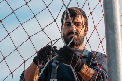 Portrait of young man looking through chainlink fence