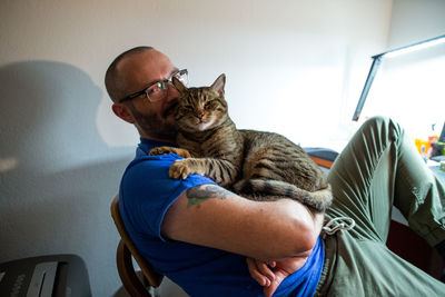 Man with glasses holds his brown tabby cat and smiles