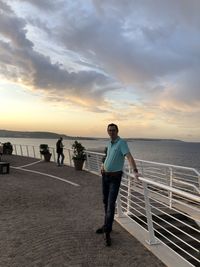 Portrait of man standing by railing against sea during sunset