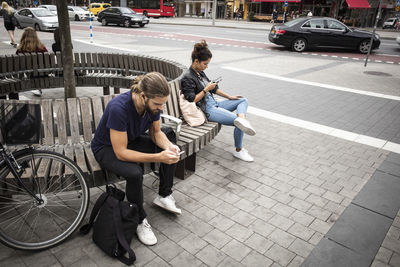 High angle view of man and woman sitting on wooden bench by city street