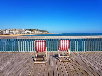  deck chairs against blue sea against clear sky