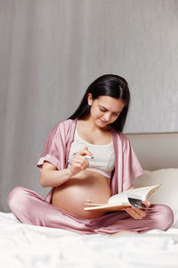 Pregnant woman writing on bed at home