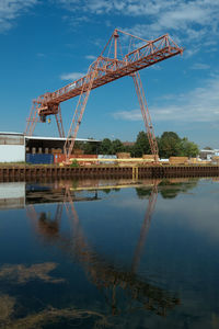 Cranes at construction site by river against sky