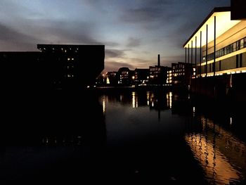 Silhouette buildings by lake against sky at night