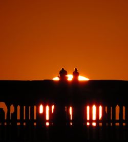 Silhouette people against illuminated orange sky during sunset