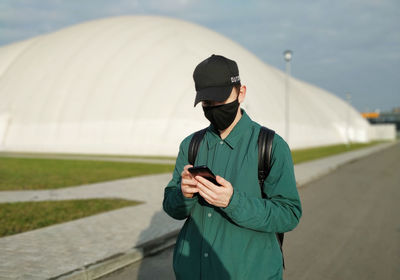 Young man using mobile phone while standing at camera