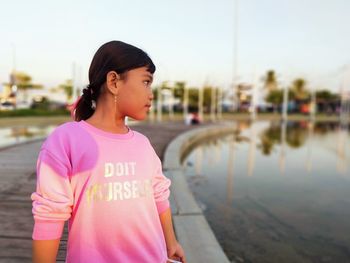 Girl looking away while standing against pink background