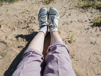 Woman's legs wearing pink pants and white sneakers laying at the beach